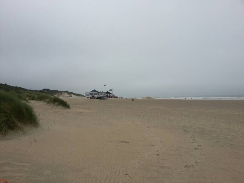 Strand mit Dünen, Gebäude am Horizont mit Flaggen, grauer Himmel über dem Meer.