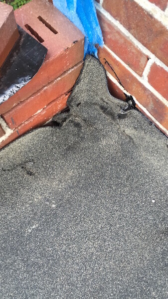 Bitumen-Dachabdichtung an Ziegelmauer mit Riss und Abdichtungsfehler