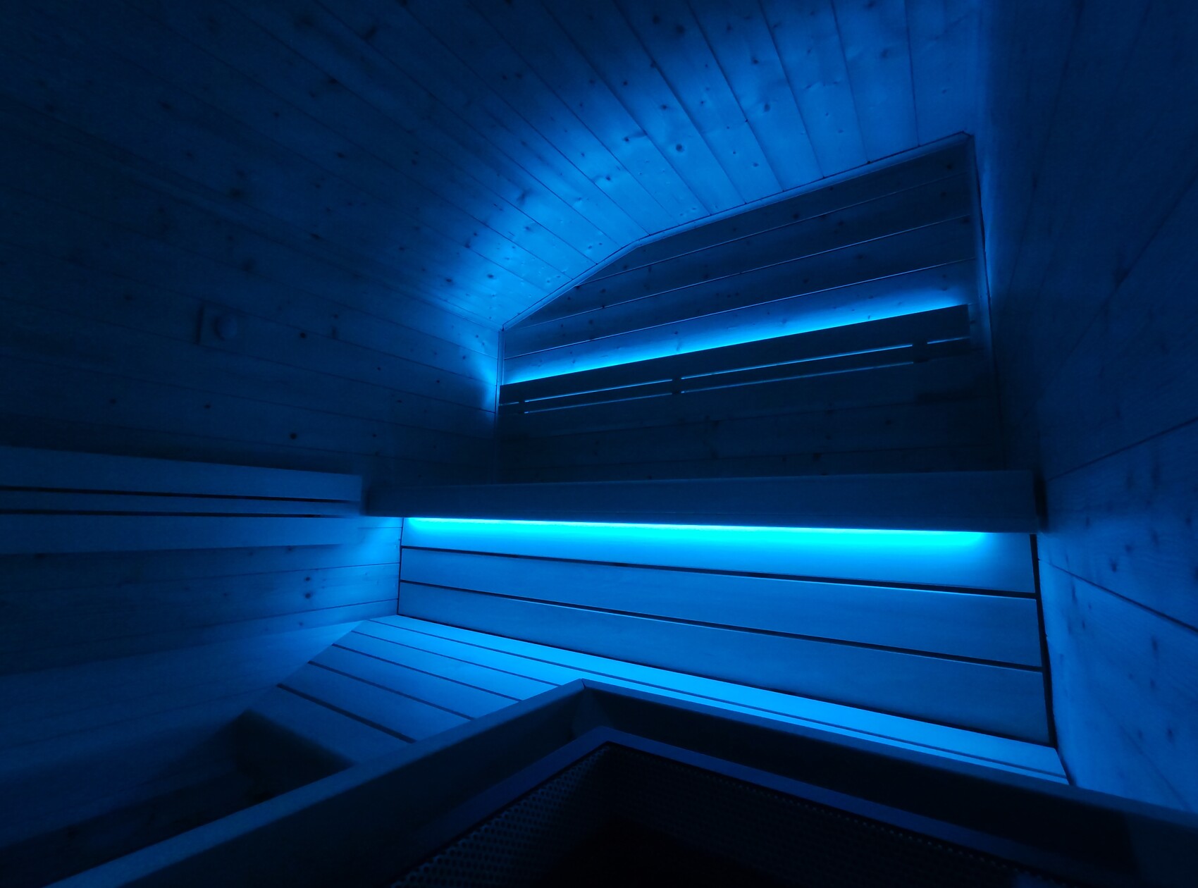 Moderner Sauna-Innenraum mit Holzwänden, blauer LED-Beleuchtung und mehreren Bänken