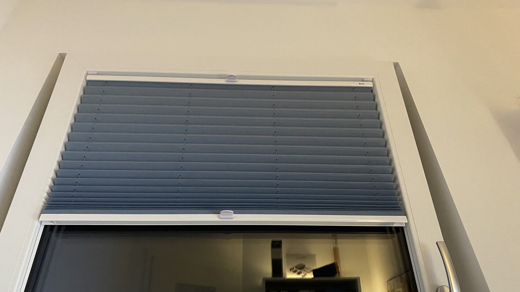 Weißer Fensterrahmen mit hellblauen horizontalen Jalousien, von innen gesehen.
