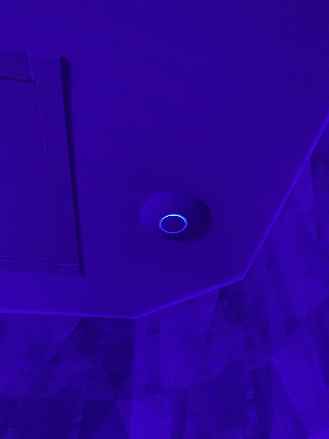 Runde Deckenleuchte mit blauem Leuchtring in violettem Licht an der Decke.