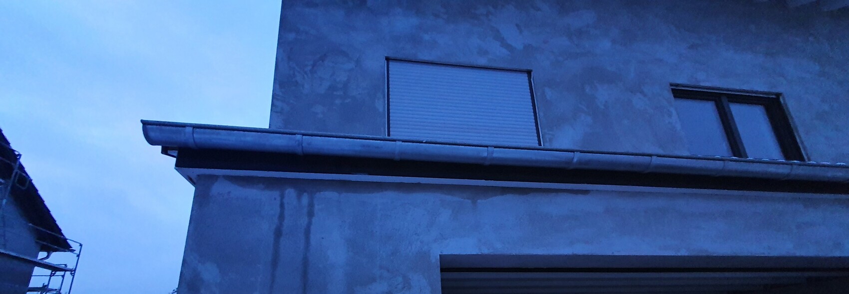 Graue Gebäudefassade mit geschlossenem Rollladenfenster und Dachrinne