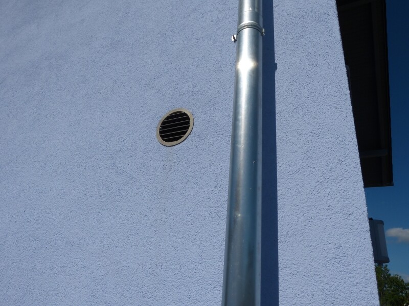 Außenwand in blauer Putzoberfläche mit runder Belueftungsöffnung und Metallrohr