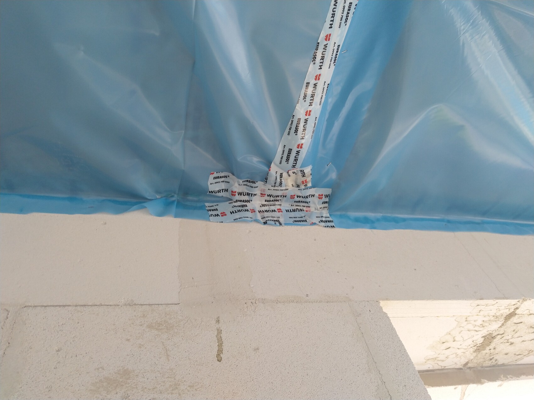 Blaue Baufolie mit Klebeband an einer Baustelle, Betonboden sichtbar