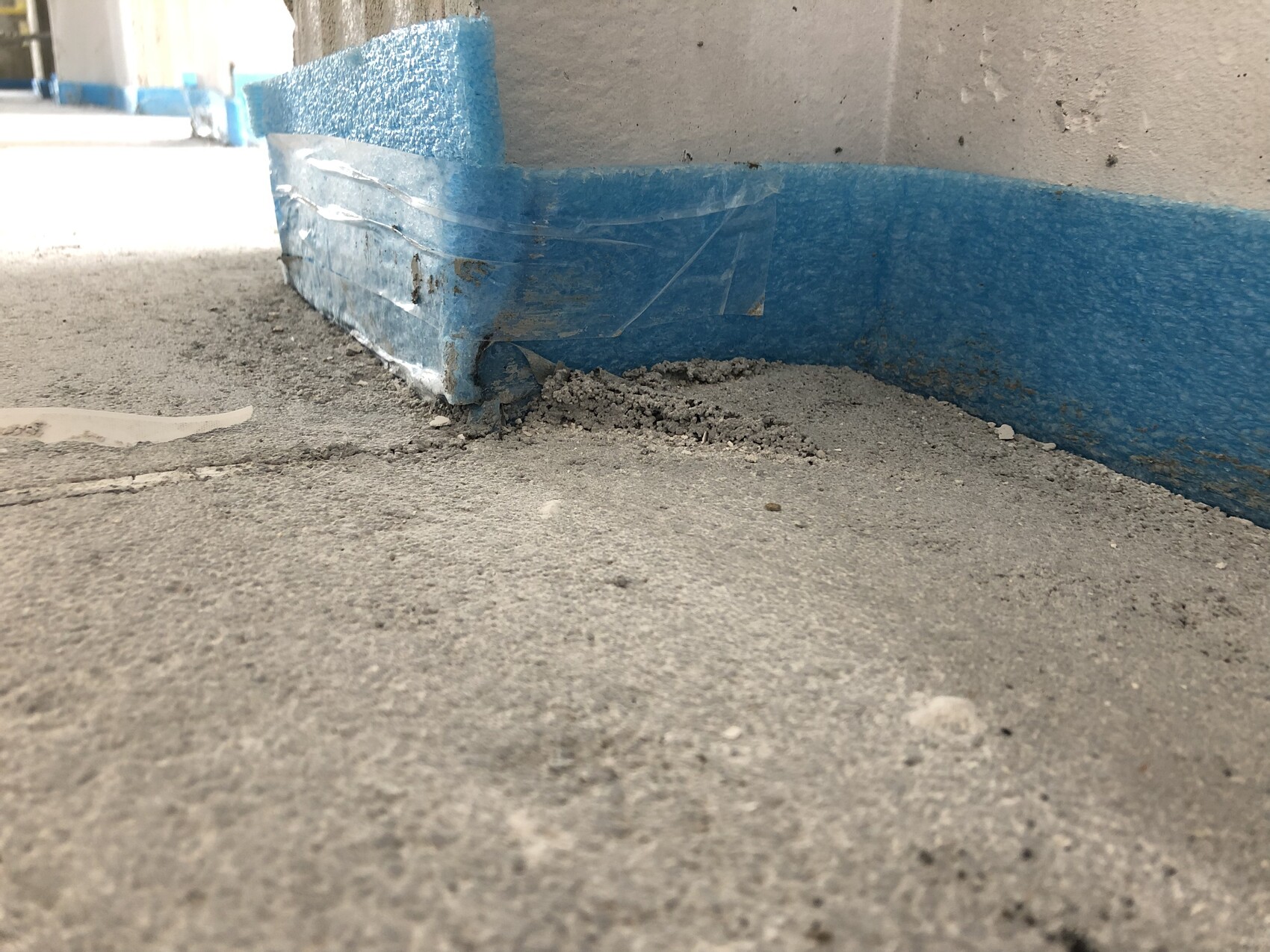 Tiefer Blick auf grauen Betonboden und blaue Schutzleiste am Wandfuß, Staubreste.