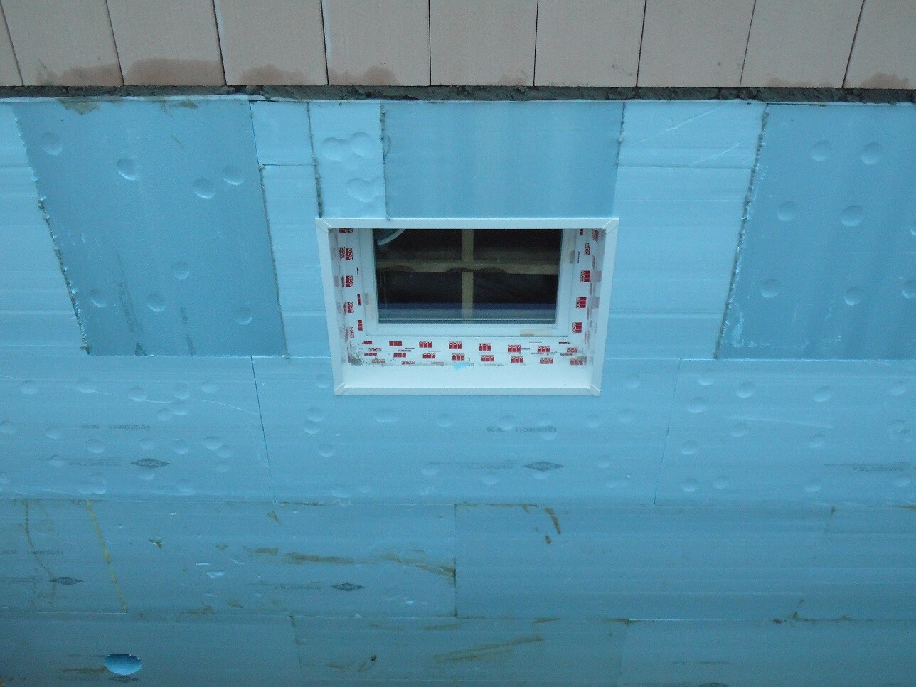 Baustellenwand mit blauen Dämmplatten und eingebautem Fensterrahmen