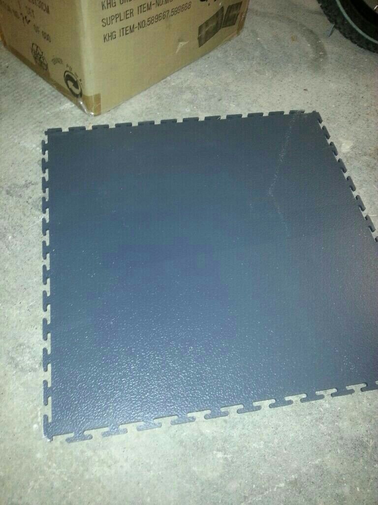 Blaues Schaumstoff-Puzzlebodenfliesen-Teil liegt auf Betonboden neben Kartonbox.