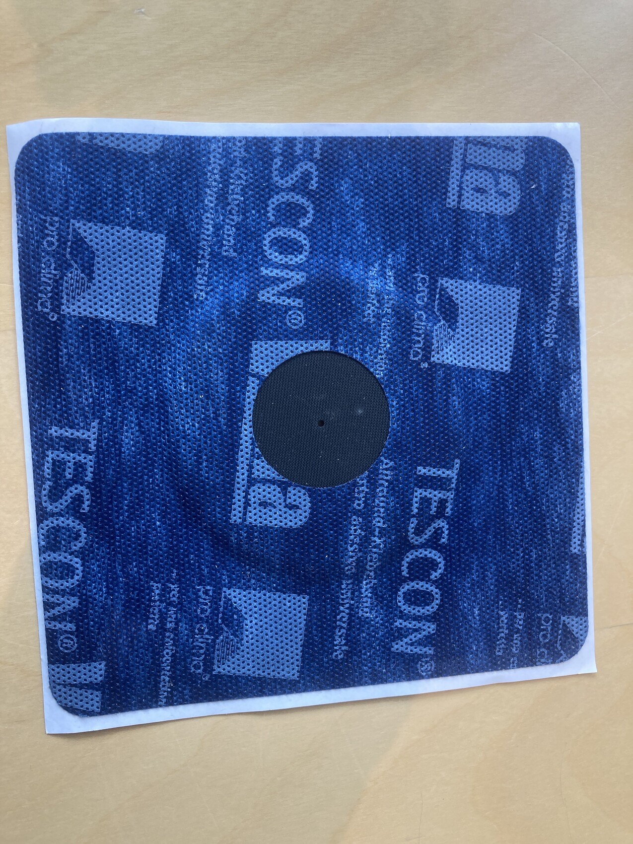 Blaues quadratisches Etikett mit Punktmuster, zentrale schwarze Scheibe mit Loch