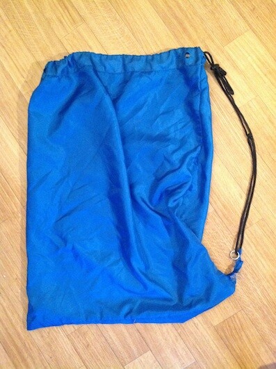 Blauer Kordelzug-Beutel aus Nylon liegt flach auf Holzboden.