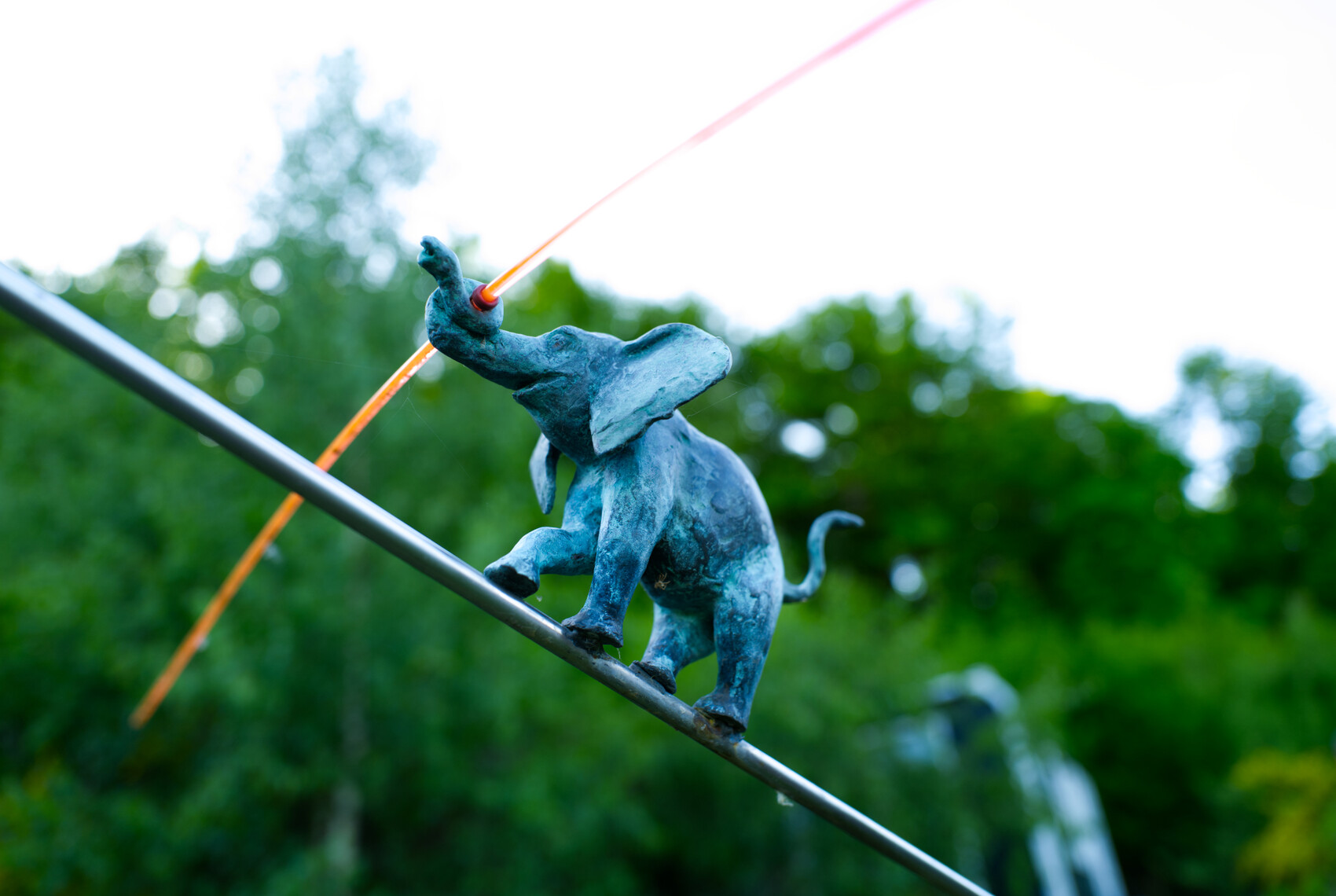 Kleine blaue Elefantenfigur balanciert auf einer Metallstange im Garten