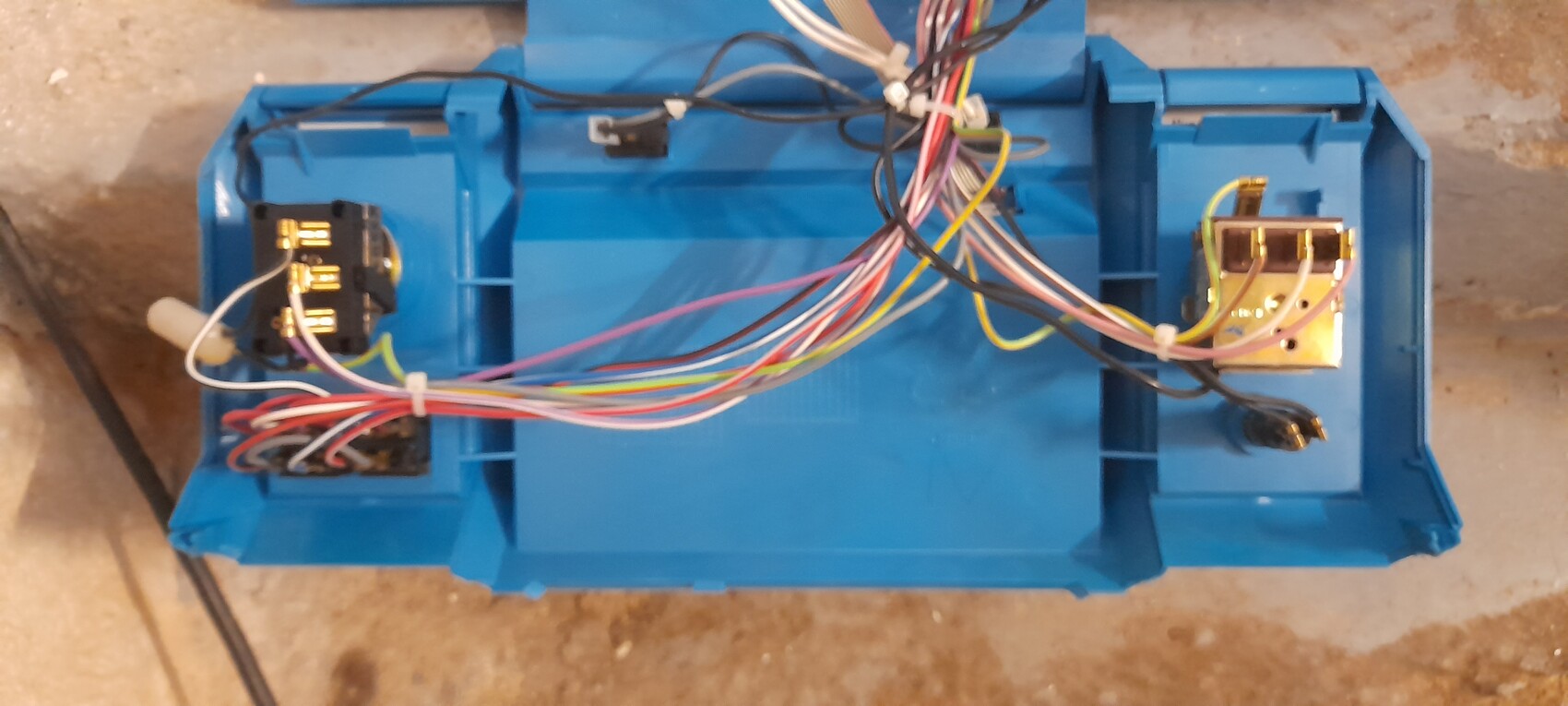 Offenes blaues Elektronikgehäuse mit vielen farbigen Kabeln, Steckverbindern und Anschlüssen.