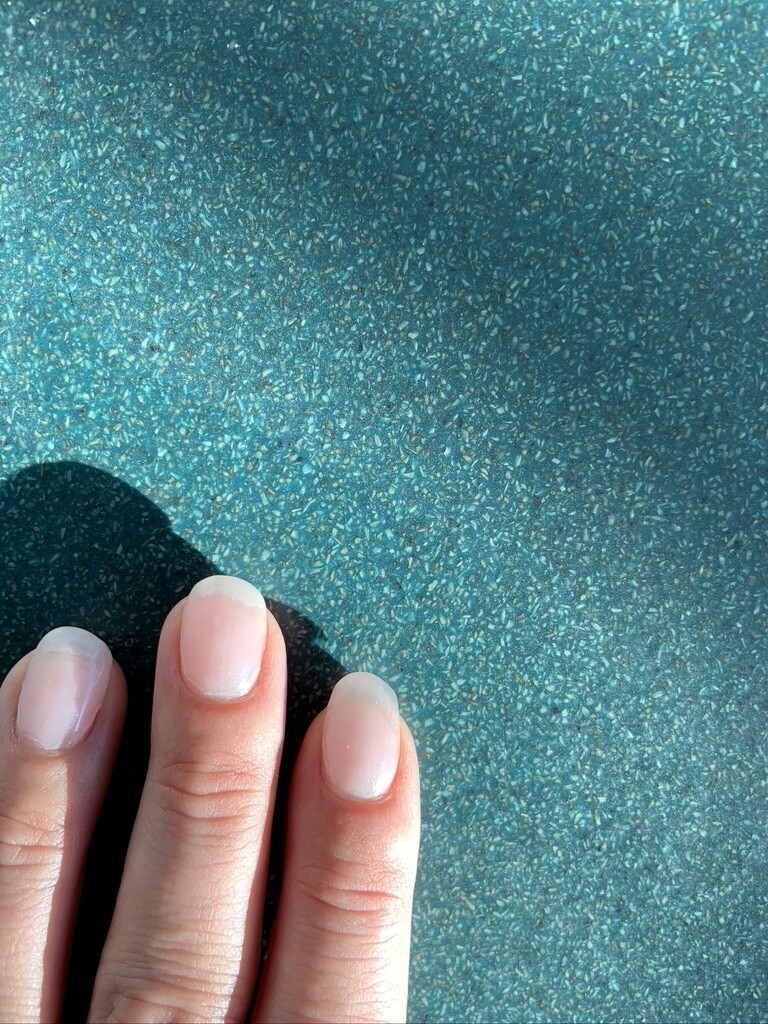 Nahaufnahme von drei Fingernägeln auf türkis-blauer, gesprenkelter Oberflächenstruktur.