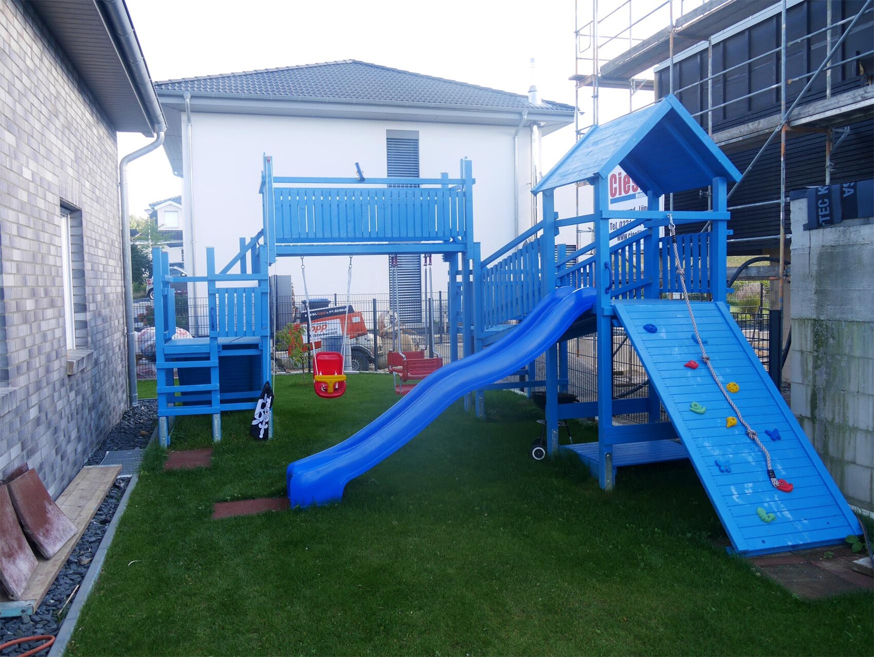 Blauer Holz-Kinder-Spielplatz mit Rutsche im Garten zwischen Häusern