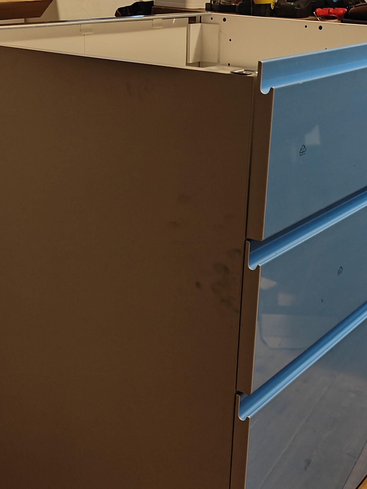 Schubladenschrank mit drei blauen Schubladen rechts und brauner Seitenwand links.