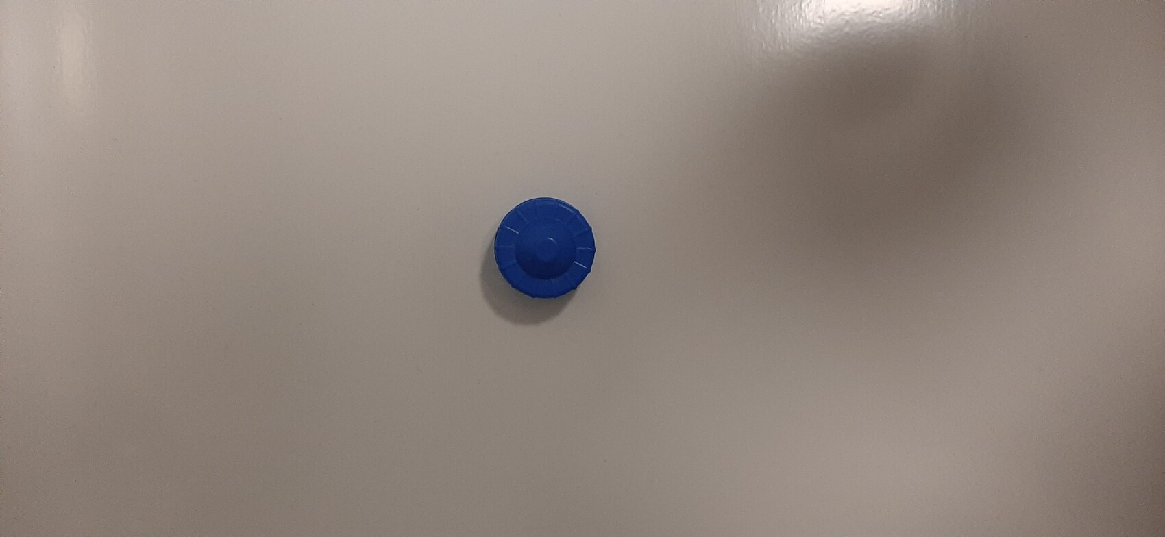 Kleiner blauer Plastikdeckel liegt auf einer glatten hellgrauen Oberfläche.