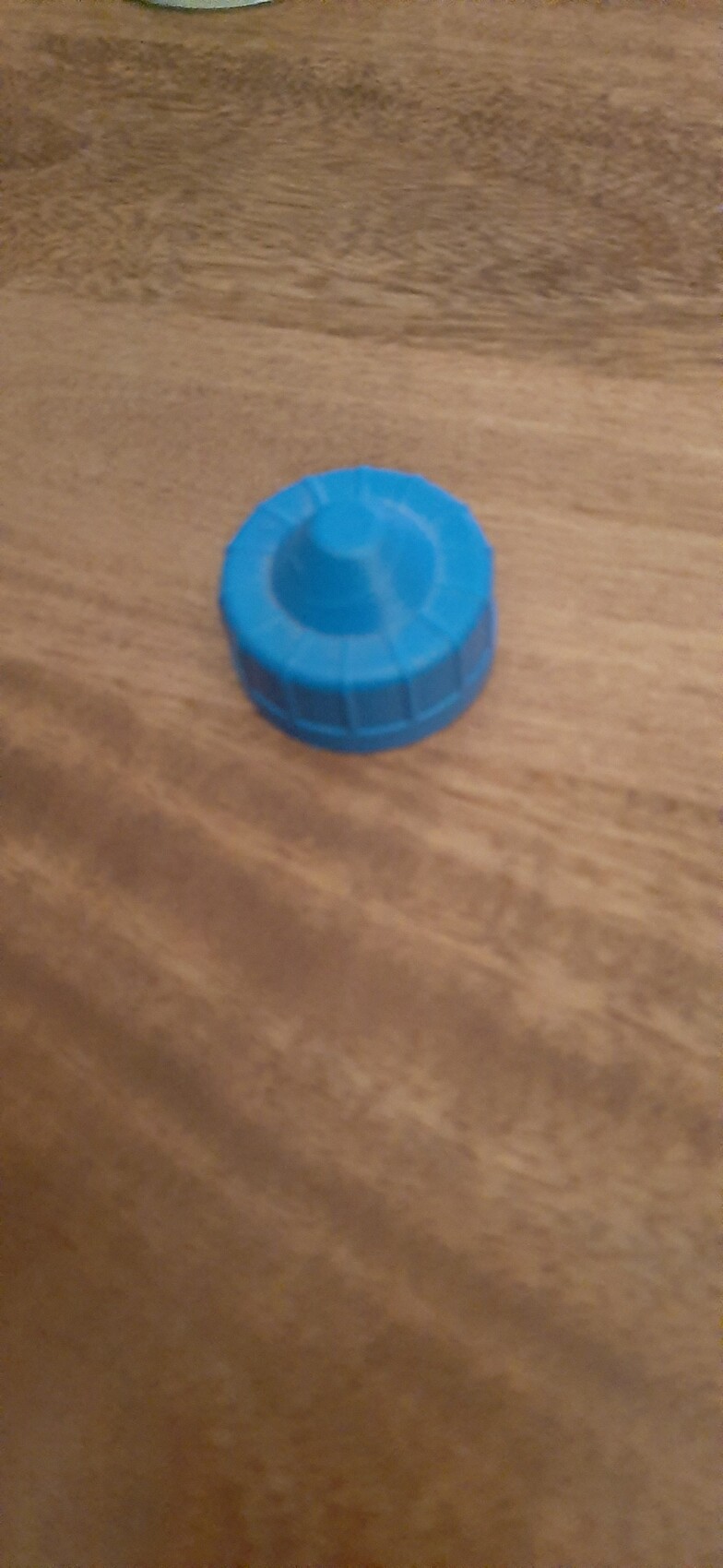 Blauer Kunststoffdeckel mit Innenzylinder, liegt auf einer Holzoberfläche.