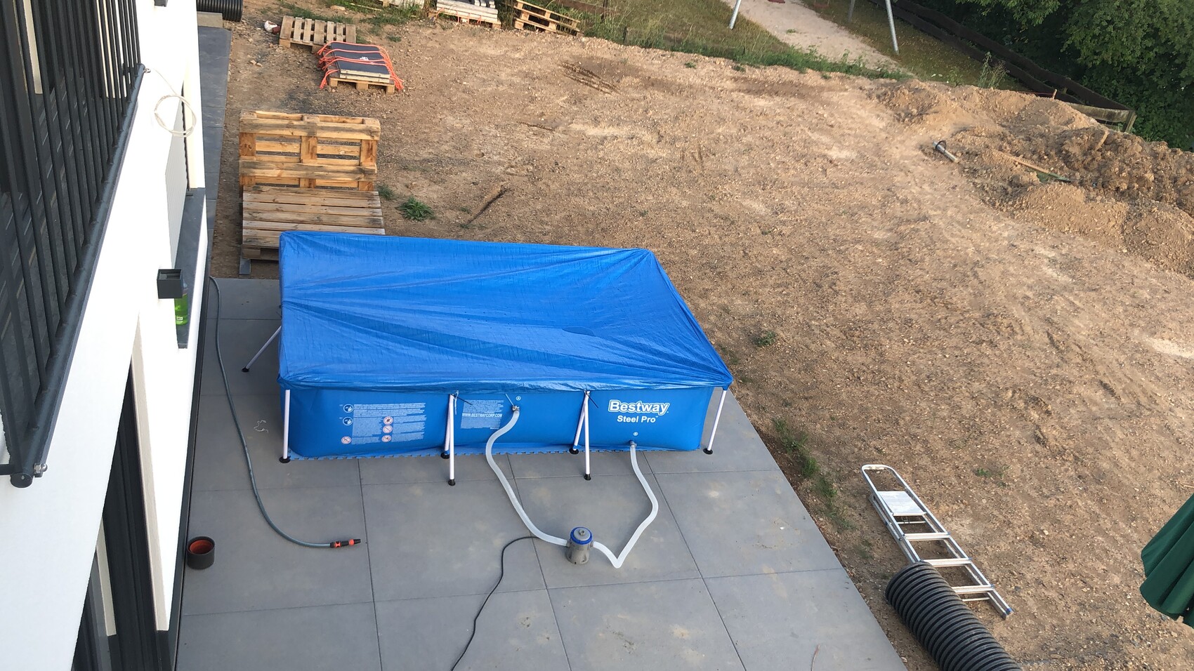Blauer Bestway Steel Pro Pool mit Abdeckung auf Terrassenfliesen, Schläuche zur Pumpe.