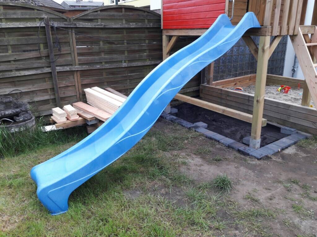Blaue Rutschbahn an einem Holzspielgerät im Garten mit Sandkasten