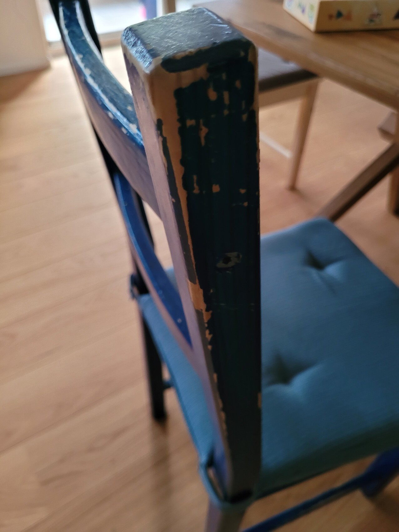 Nahaufnahme eines blauen Holzstuhls mit abgeblätterter Farbe, Holz darunter sichtbar.