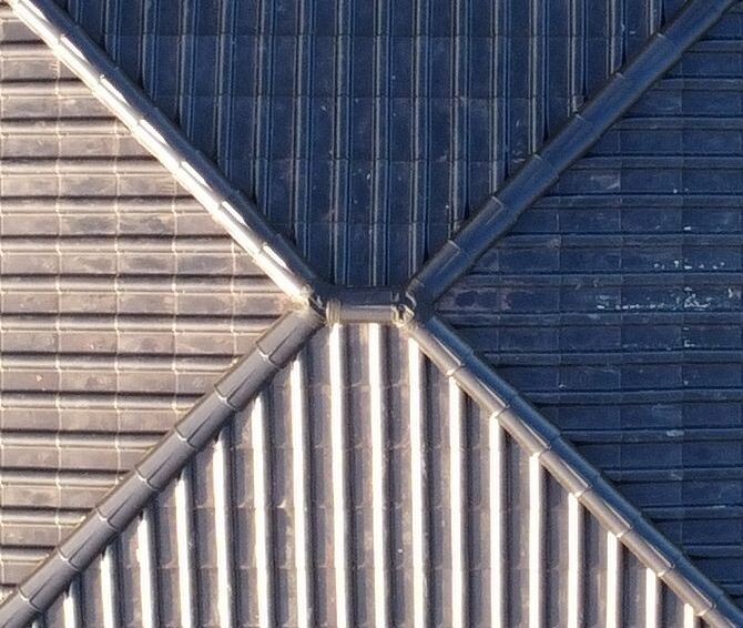 Nahaufnahme eines Daches mit kreuzförmiger Metallverbindung zwischen Dachflächen.