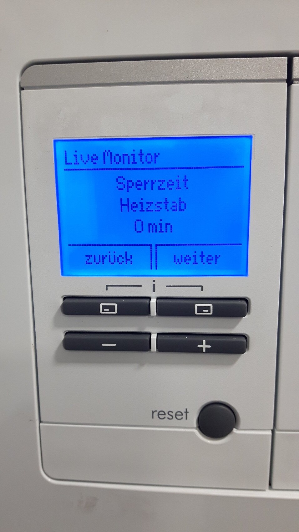 Nahaufnahme eines Heizungsbedienfelds mit blauem Display: Live Monitor, Sperrzeit 0 min, Zurück/Weiter