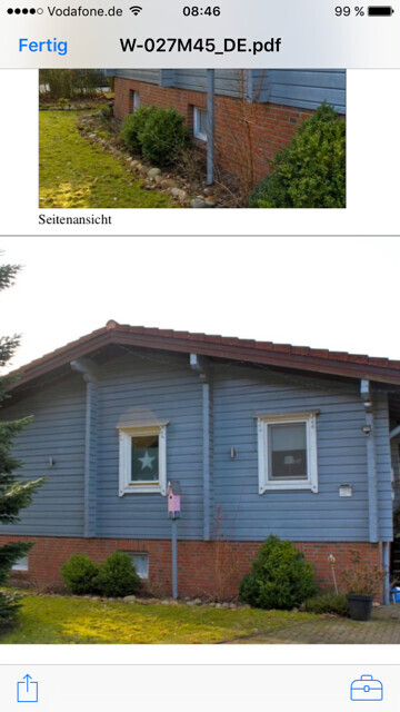Außenansicht eines blauen Holzhauses mit Fenstern, Ziegelgrundmauer und Garten.