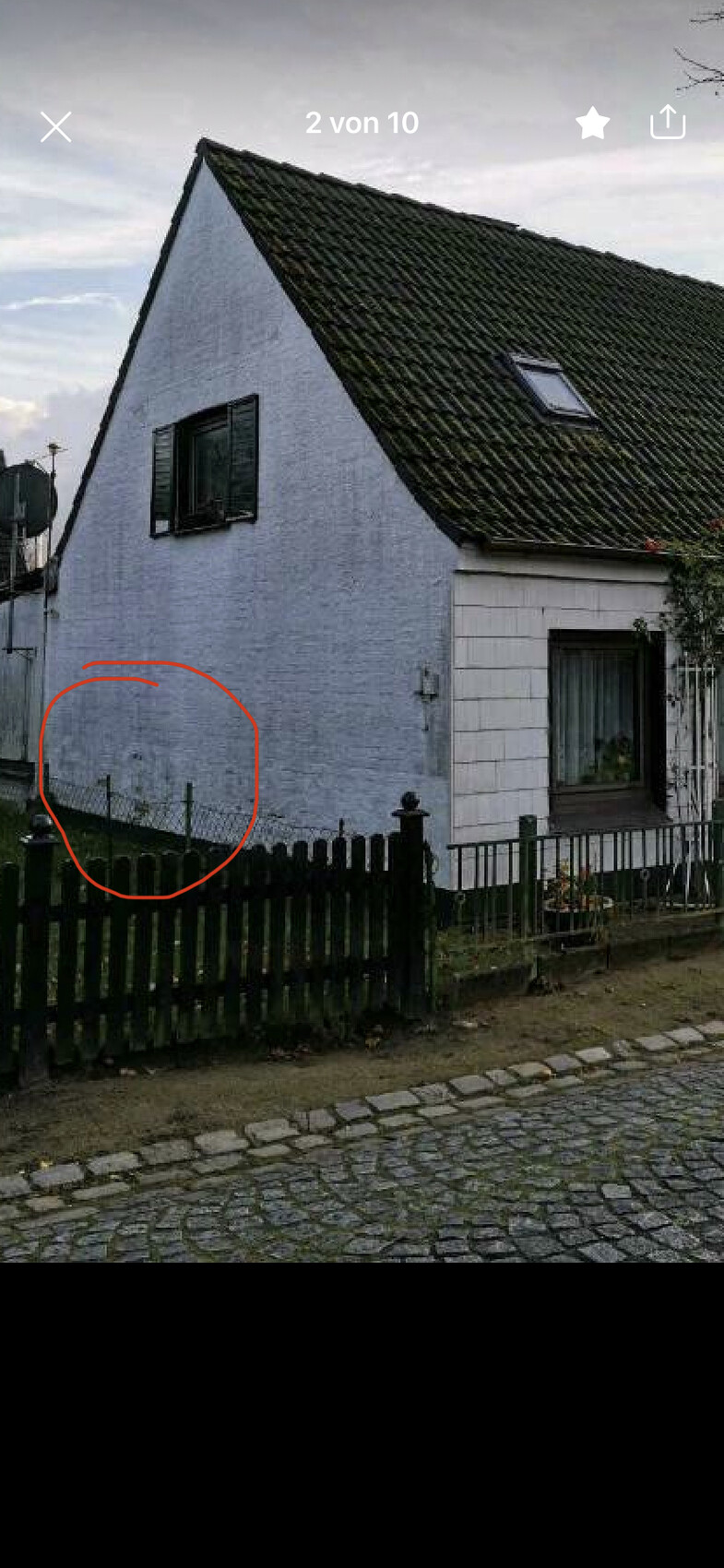 Blaues Einfamilienhaus mit steilem Dach, Fenster, Dachfenster, Gartenzaun und Kopfsteinpflaster.
