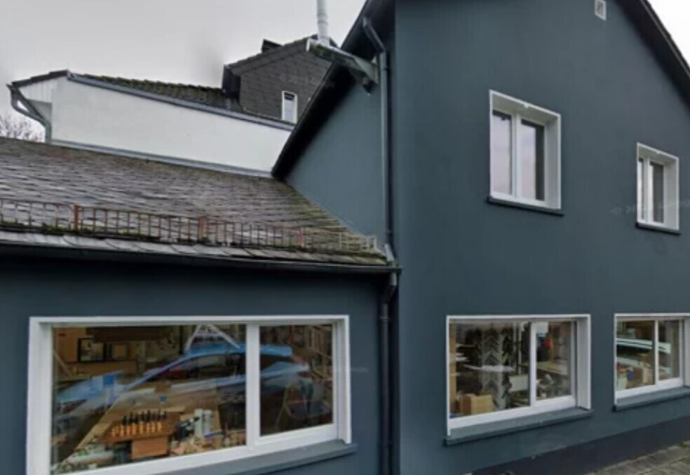 Blaues Haus mit großen Fensterfronten; Innenräume hinter den Scheiben sichtbar.