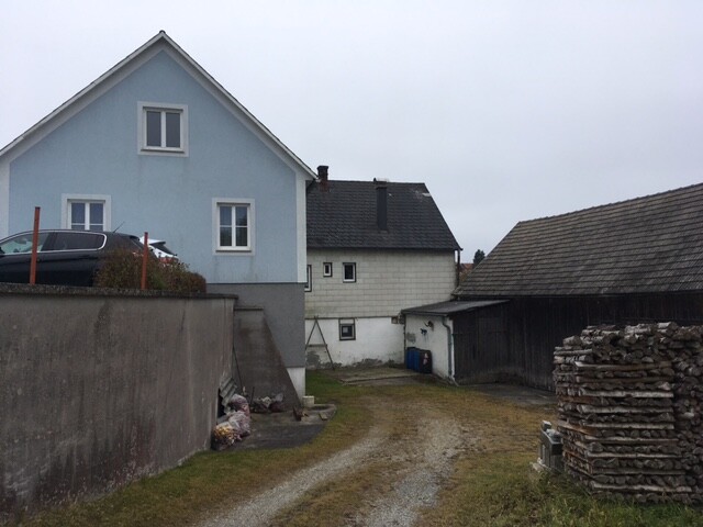 Außenansicht eines blauen Hauses mit Hof, Nebengebäuden und Holzstapel
