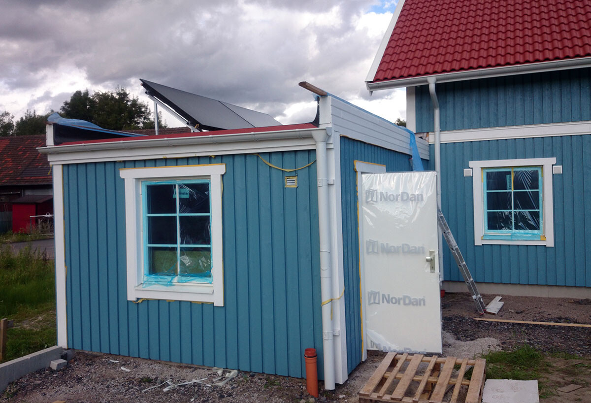 Außenansicht eines blauen Holzhauses im Bau mit Fenstern und Tür auf einem Baugelände