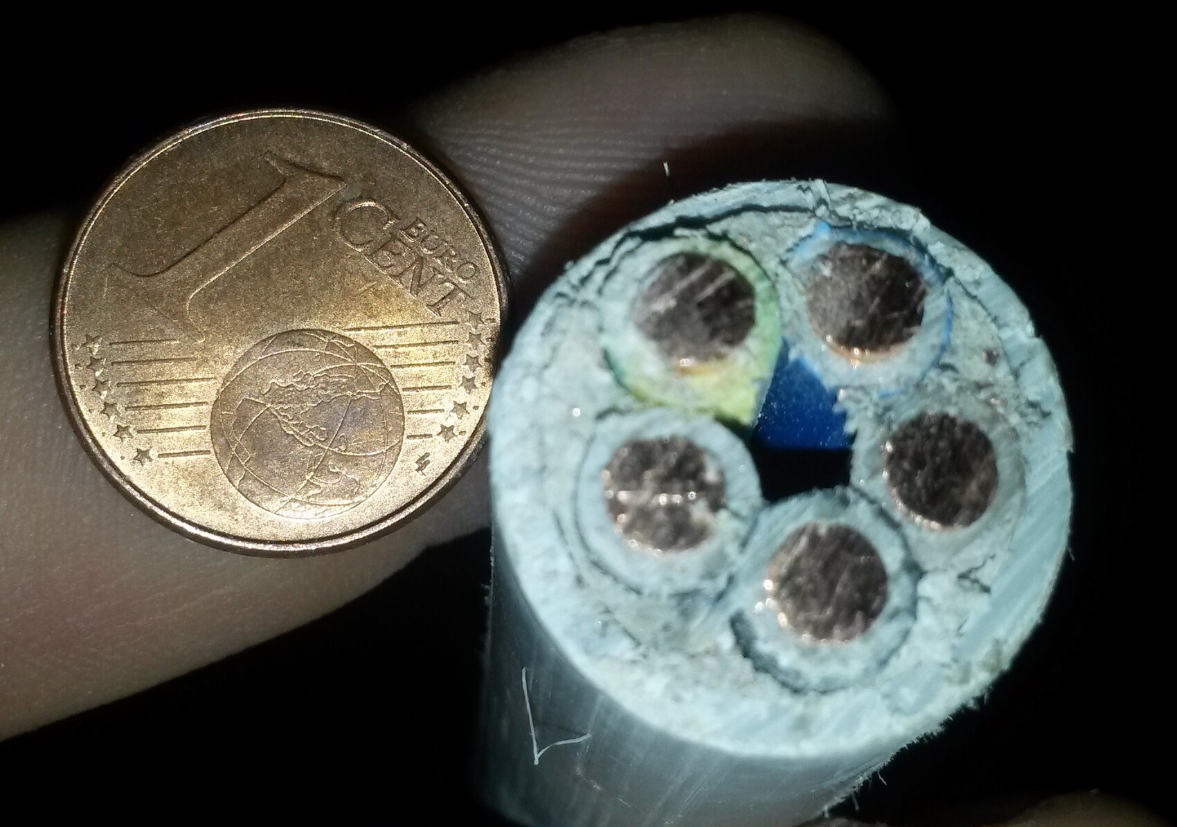 Nahaufnahme eines blauen Kabelquerschnitts mit mehreren Drähten neben einer 1-Euro Münze.