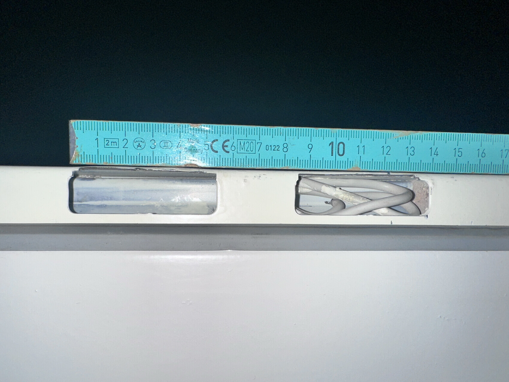 Blaues Messband liegt über einer weißen Oberfläche; rechts Kabel im Schlitz sichtbar.