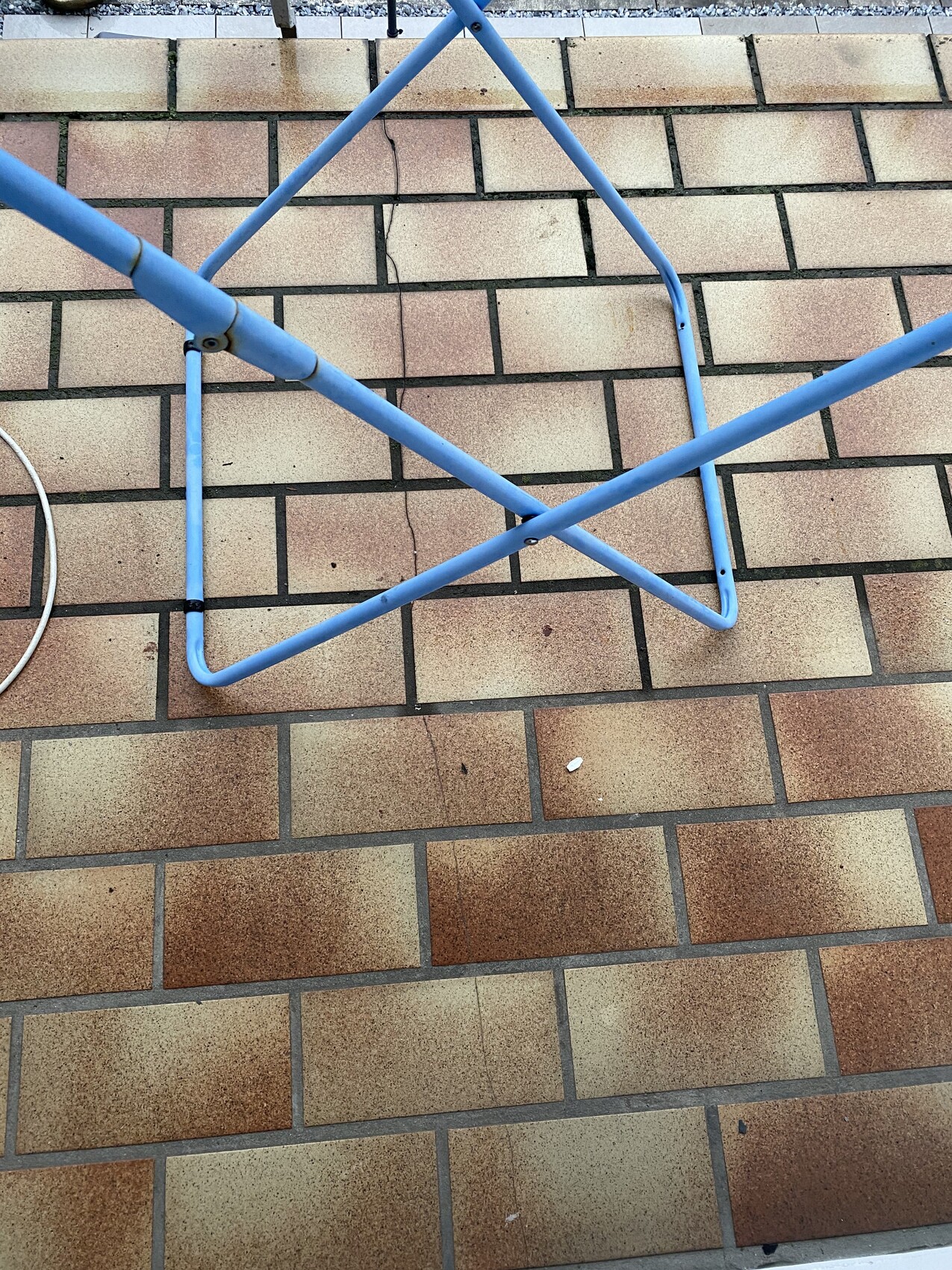 Blaues Metallrohr-Gestell liegt flach auf beigen Fliesen; Rahmen bildet ein Quadrat.