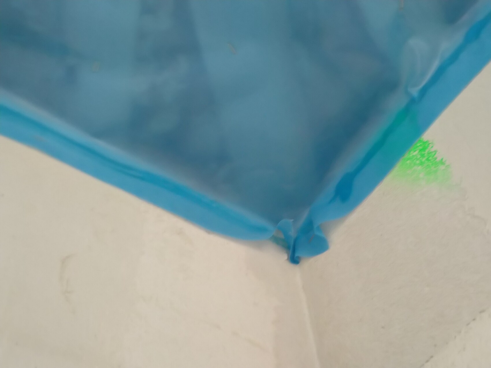 Nahaufnahme einer blauen Plastikfolie in einer Gebäudeecke neben einer weißen Wand.