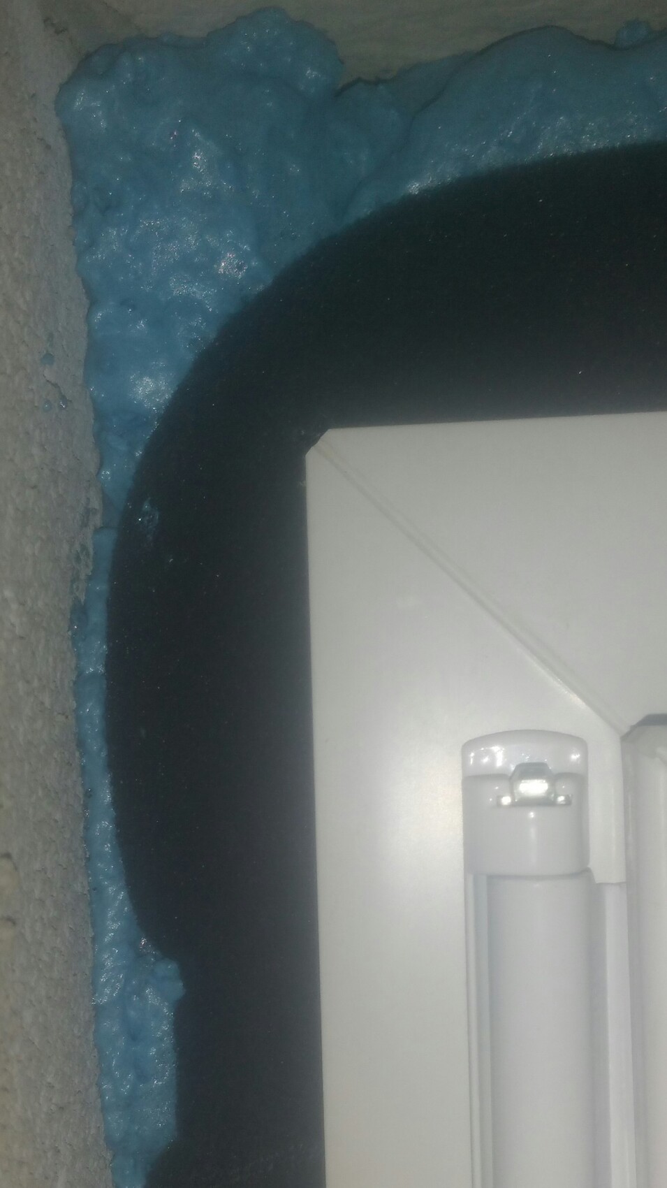 Nahe Aufnahme: blaue Schaumdämmung um runde Öffnung, weißes Kunststoffbauteil im Vordergrund