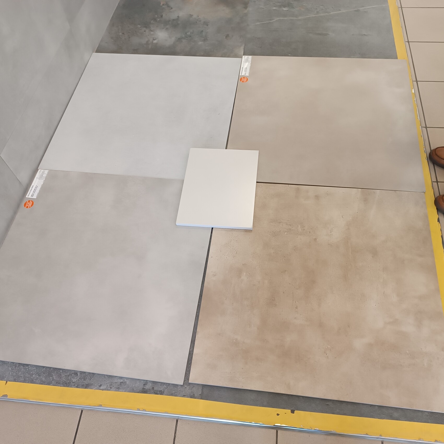 Großformatige Bodenfliesen in Grau- und Beigetönen, mittig eine weiße Fliese auf Ausstellungsfläche.