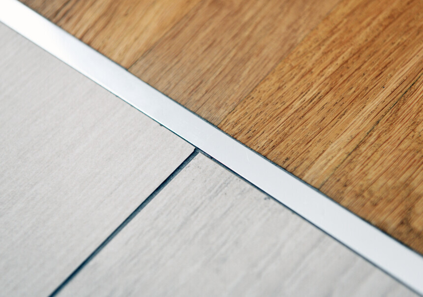 Übergang zweier Bodenbeläge: hellgraues Laminat neben braunem Holzboden mit silberner Metallleiste