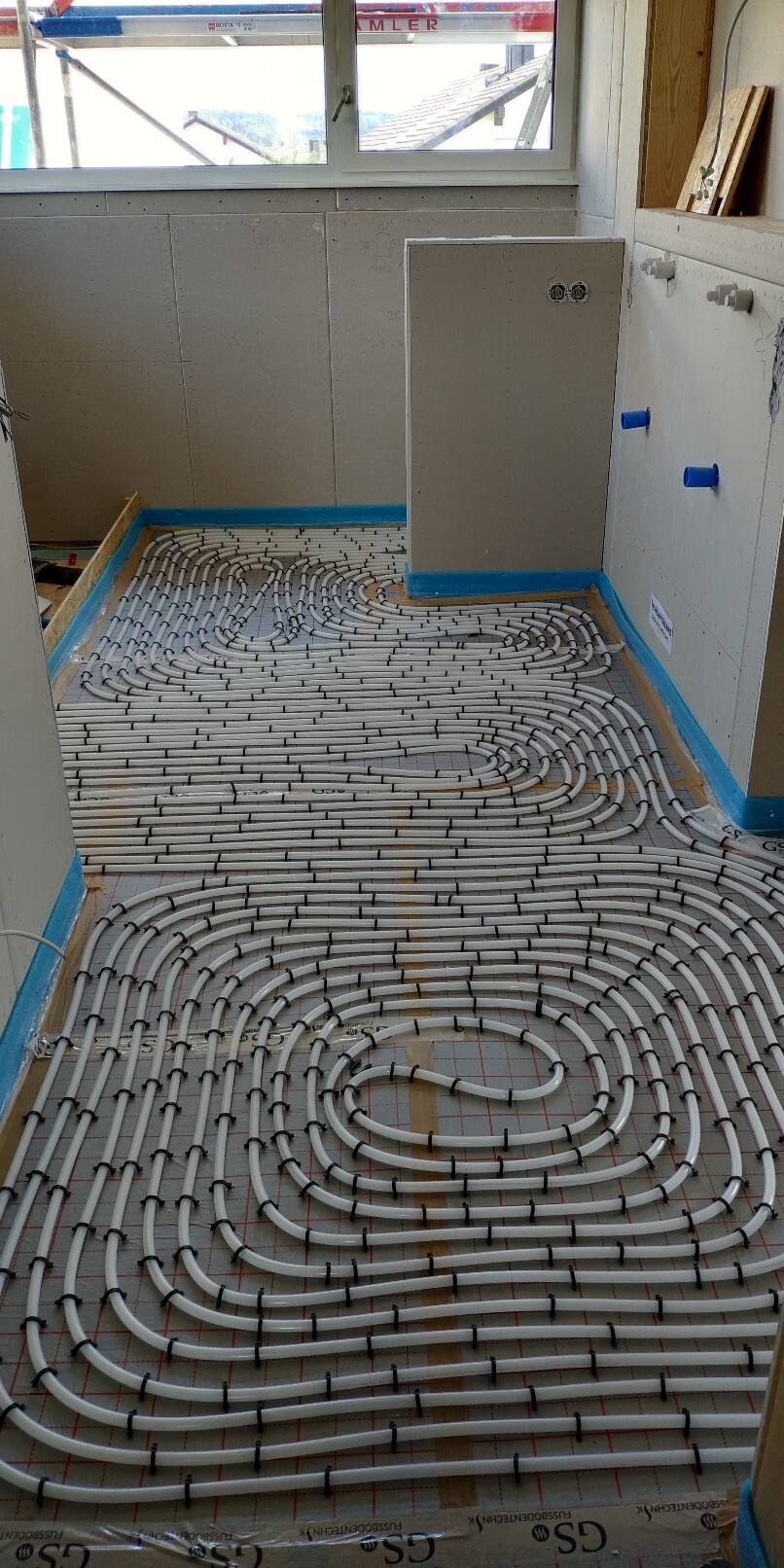 Unterbodenheizung: weiße Rohre spiralförmig auf Dämmung im Bauzimmer verlegt.