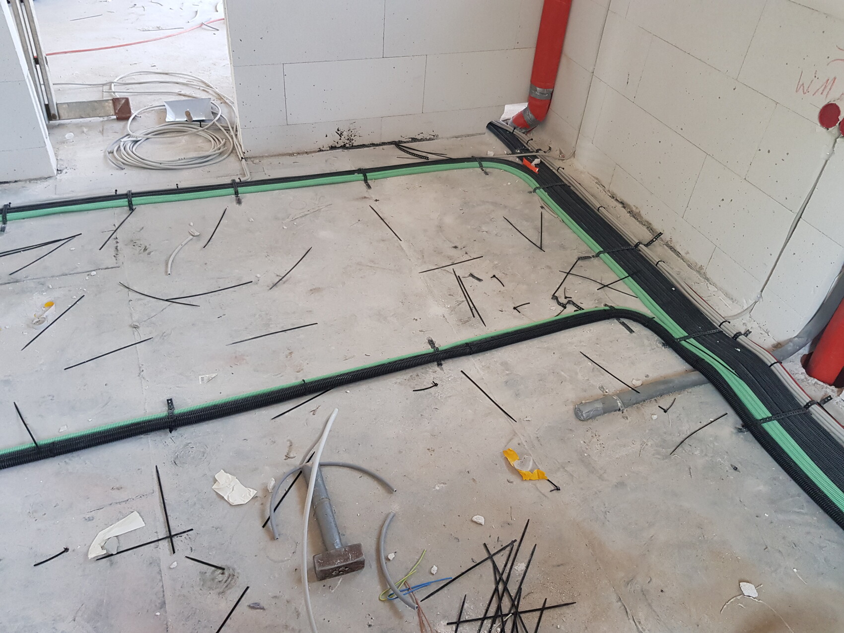 Baustelle: Boden mit Kabelkanälen, grüne Rohre, schwarzer Kabelschlauch und Werkzeuge.