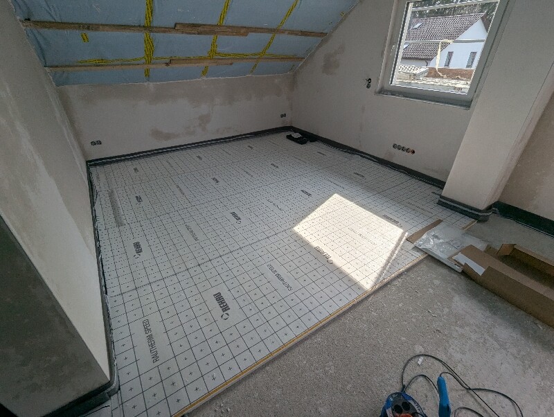 Rohbauraum mit Boden-Isolierplatten, Dachschräge, Fenster, Werkzeug liegt bereit.