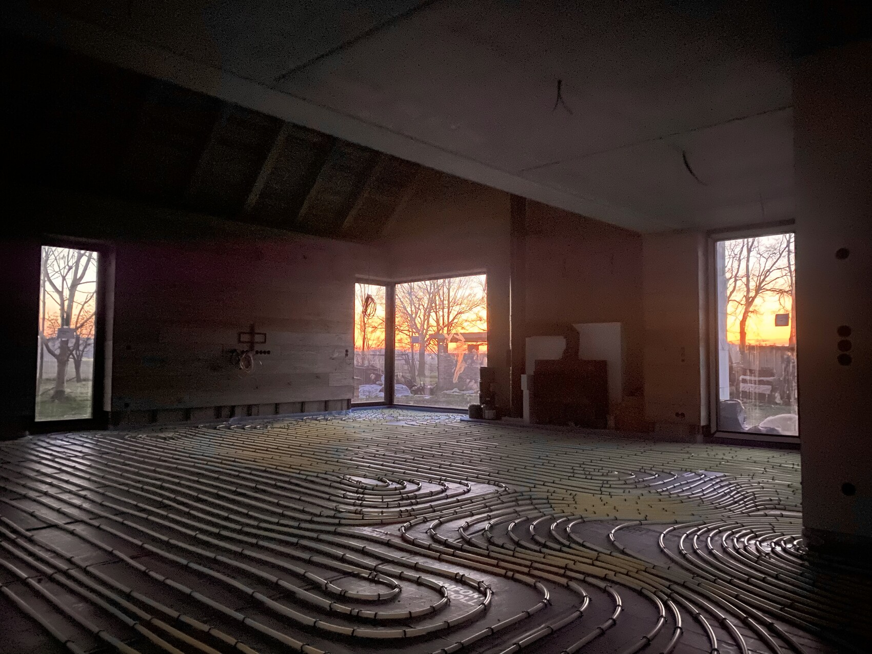 Innenraum mit Bodenheizungsrohren in Spiralen, Blick durch Fenster auf Sonnenuntergang.