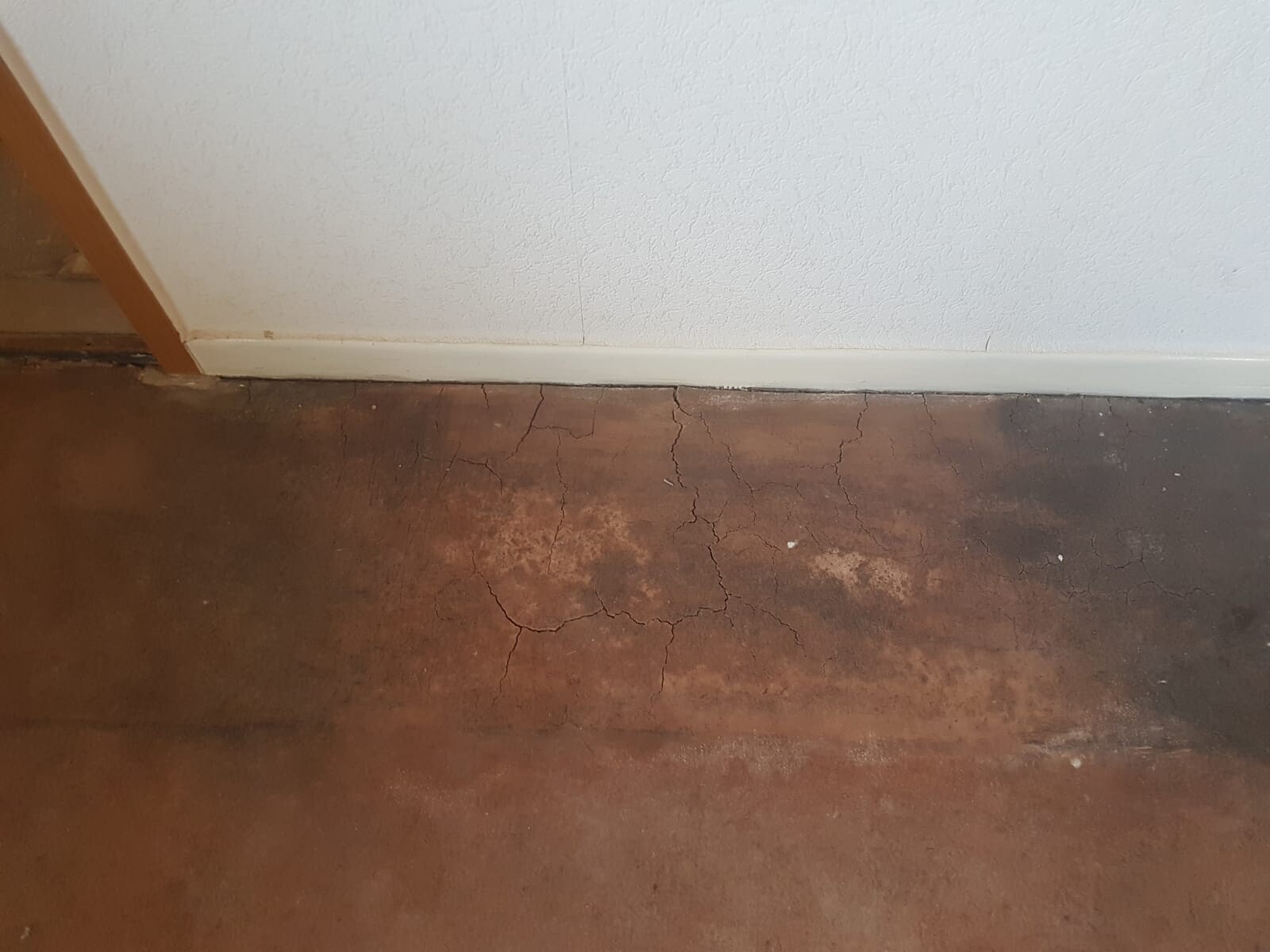 Kellerboden mit Rissen und beschädigter Oberfläche neben weißer Wand und Sockelleiste