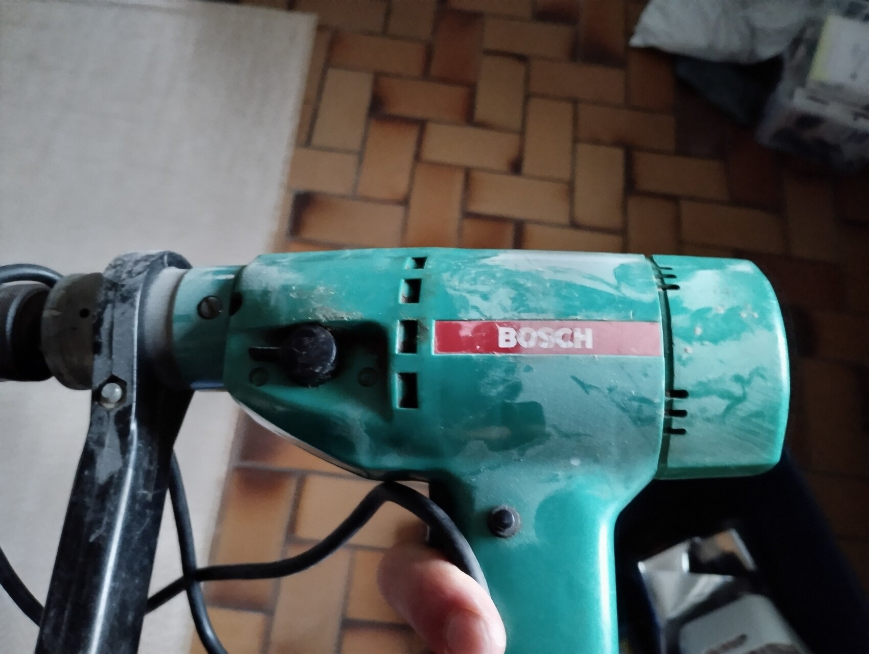 Bosch-Bohrmaschine mit grünem Gehäuse, Griff und Kabel auf Fliesen.