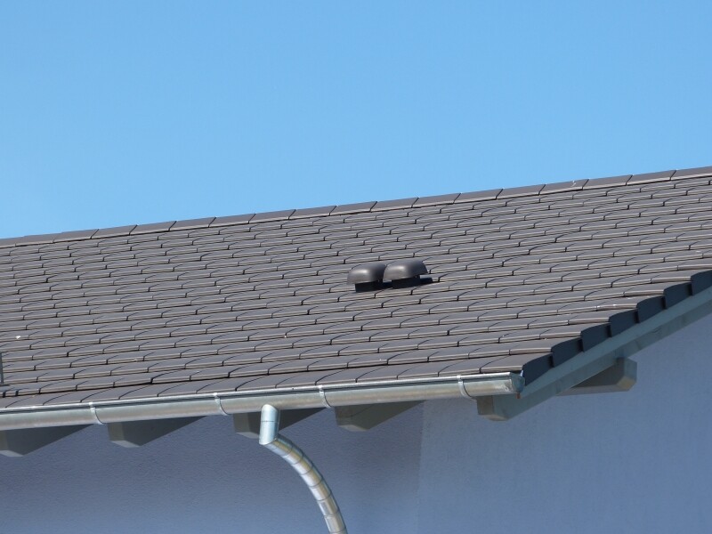 Dach mit braunen Ziegeln, Dachrinne und blauem Himmel.