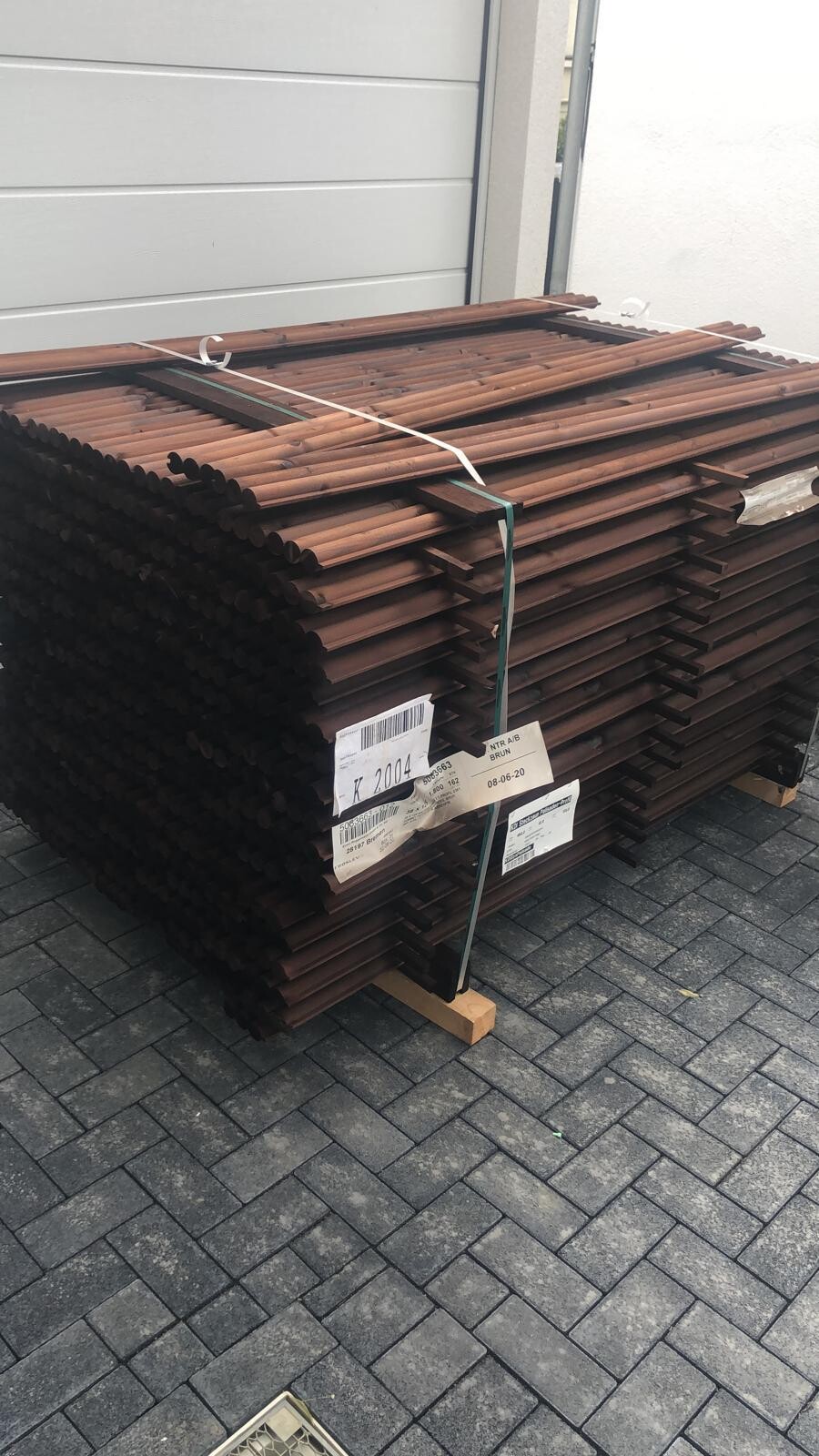 Stapel rostbrauner Stahlstangen auf Paletten, mit Gurten fixiert, neben einer Gebäudewand.