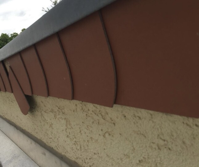 Nahaufnahme einer braunen Fassadenverkleidung mit halbrunden Paneelen über einer rauen beige Wand.
