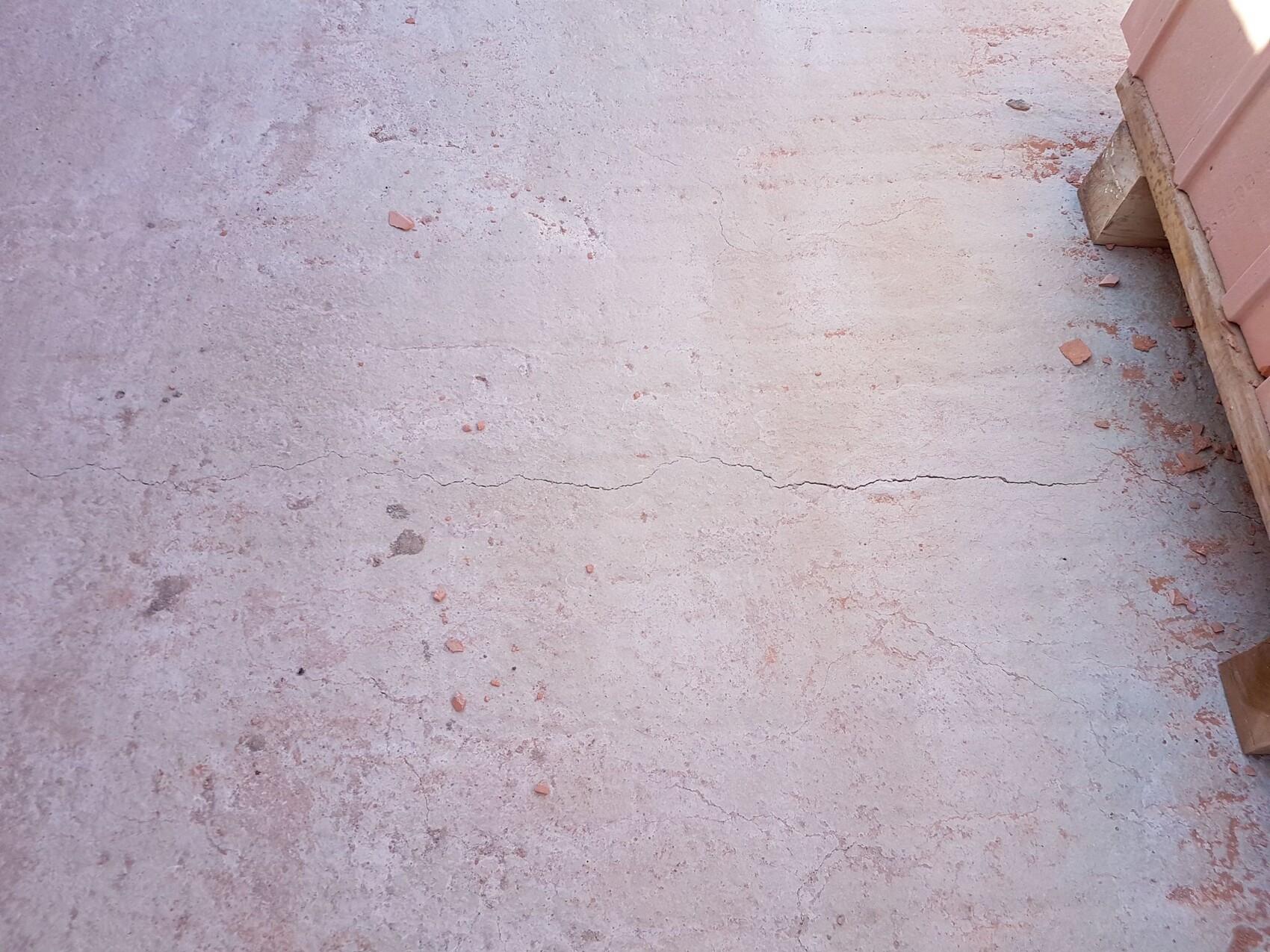 Betonboden mit Rissen auf einer Baustelle, Bauholz und Ziegelreste am Rand.