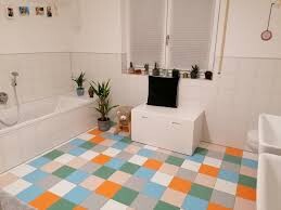 Badezimmer mit bunten quadratischen Fliesen, Badewanne links, weißer Unterschrank und Pflanze