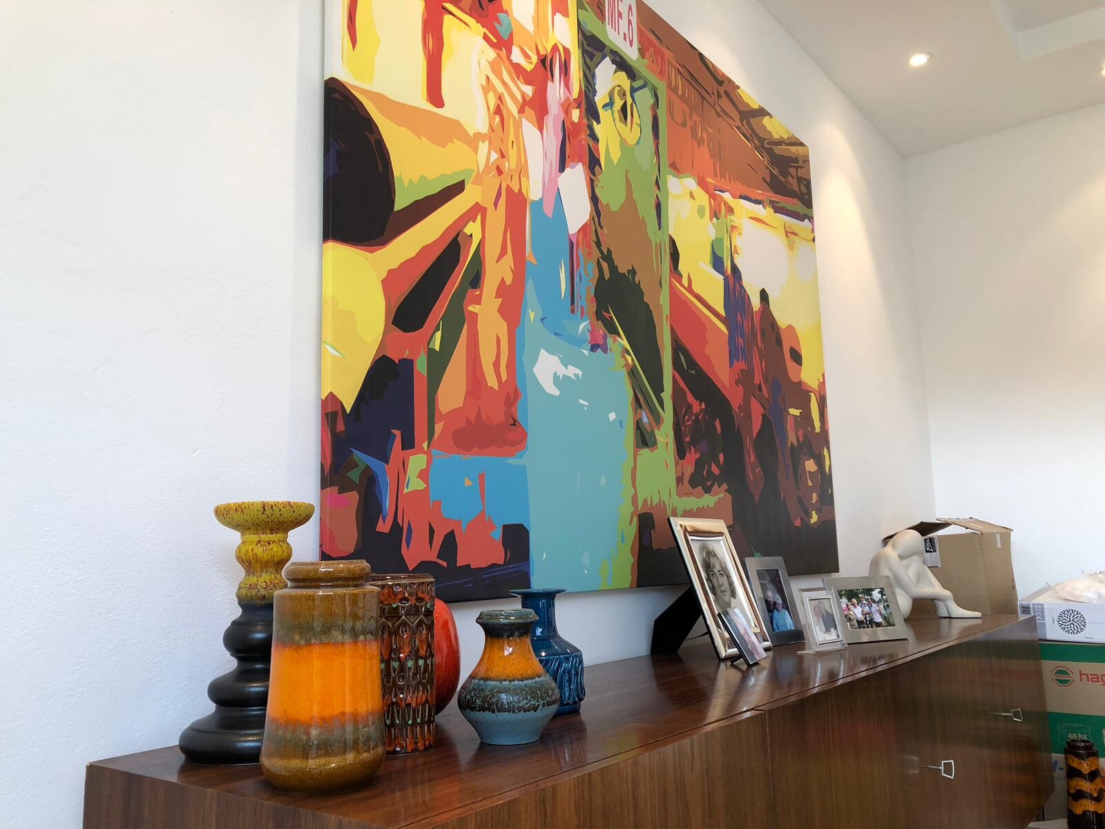 Großes farbiges abstraktes Gemälde über Sideboard im Wohnzimmer mit Vasen und Fotos.