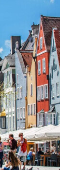 Bunte Häuserzeile an belebter Straße mit Cafés im Freien und blauem Himmel.
